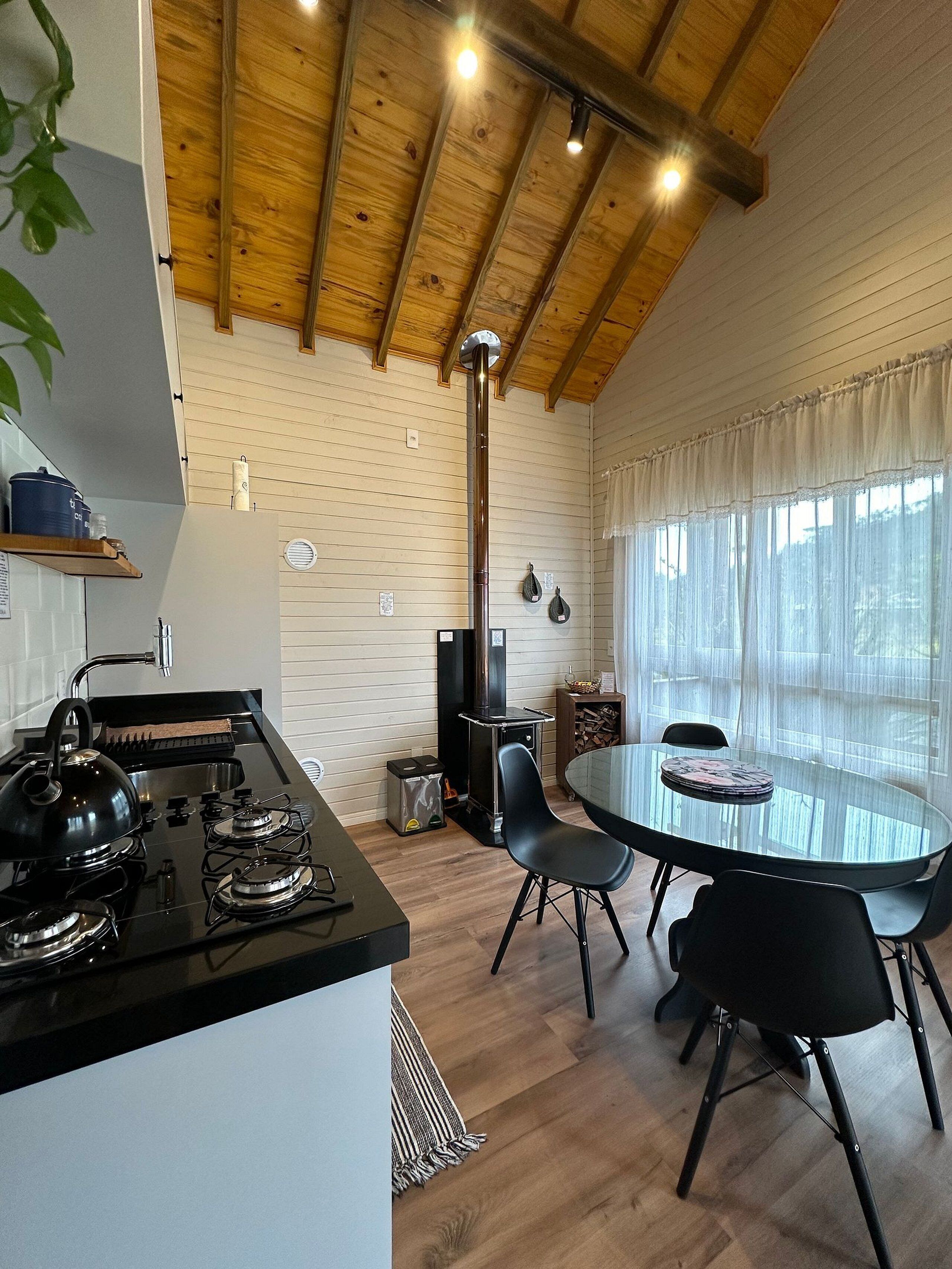 A modern kitchen with a gas stove, a black countertop, and a wooden ceiling. There is a round glass table with chairs in the dining area.