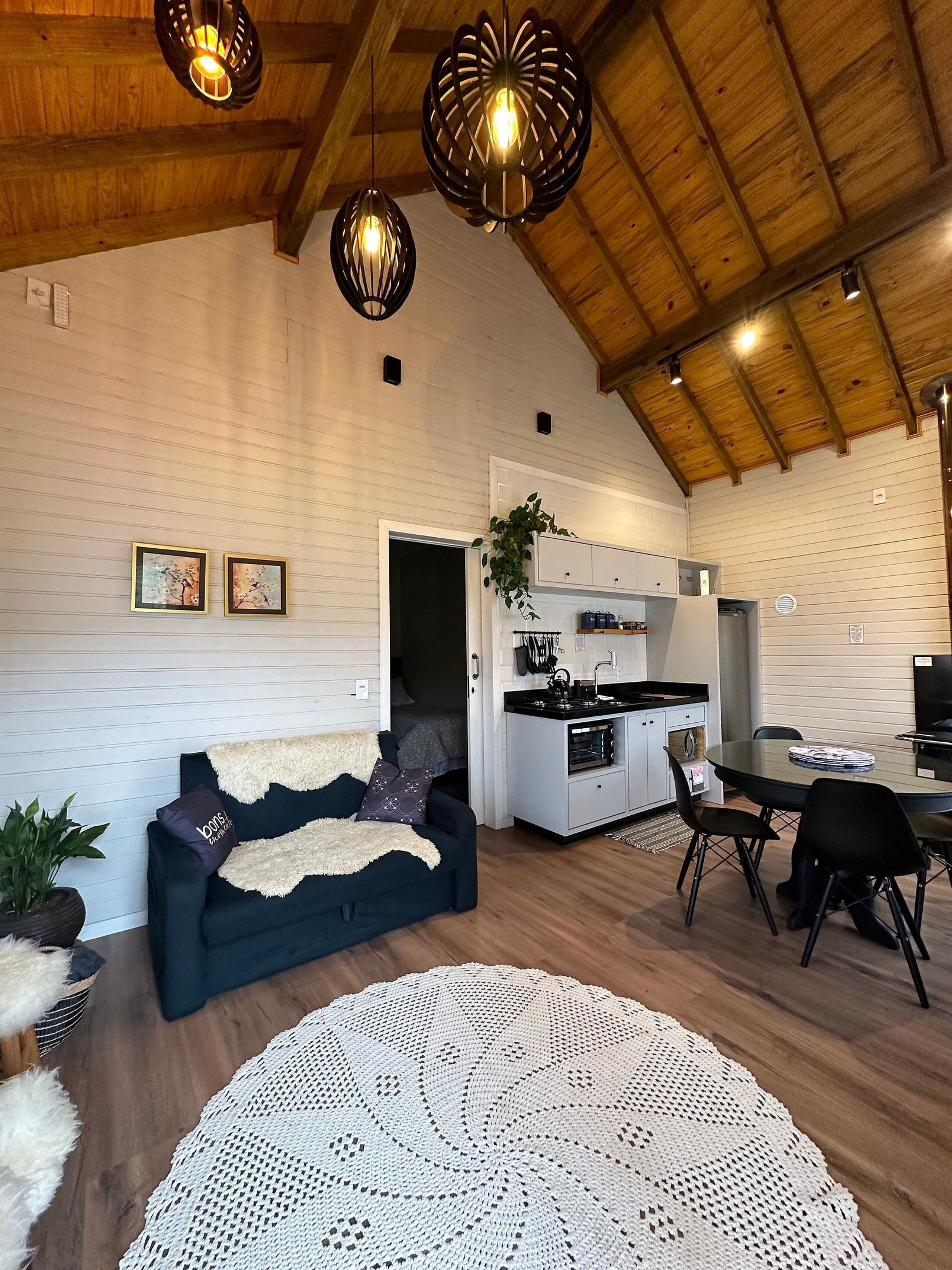 A spacious living area with a dark blue sofa, a white knitted rug, and a kitchen area with white cabinets and a dining table.