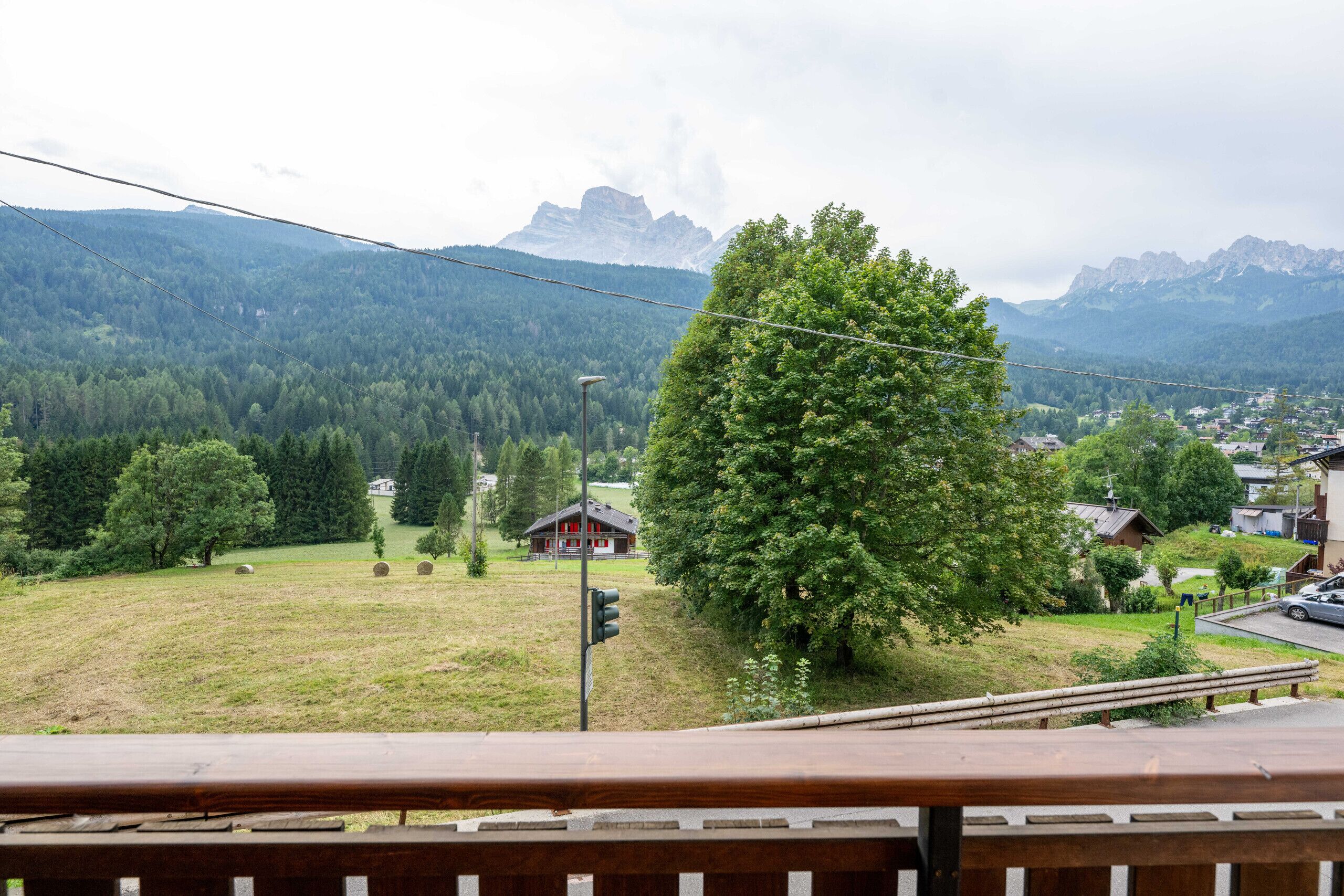 Panoramica di un paesaggio montano con un albero in primo piano, una casetta e una strada con un guardrail.