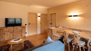 A cozy living room with a wooden TV stand, a dining table with chairs, and a sofa. - Pelmo Mountain Lodge (Borca di Cadore)