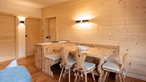 A wooden dining area with a table and chairs, a bench, and a wall-mounted light fixture. - Pelmo Mountain Lodge (Borca di Cadore)