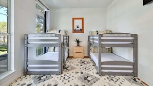 Una habitación con literas, un ventilador de techo, una pequeña mesa con una planta y un cuadro en la pared.