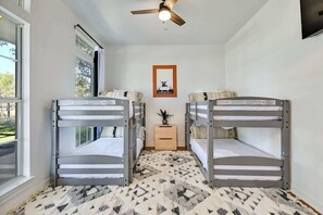 A room with bunk beds, a ceiling fan, a small table with a plant, and a framed picture on the wall. - Luxury Dripping Springs Home-Pool&Hot-Tub Firepit! (Dripping Springs)