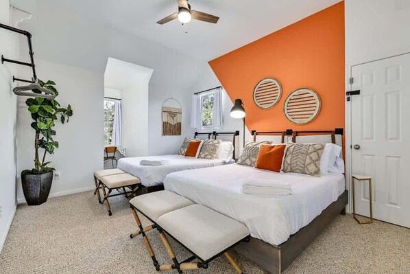 A bedroom with two beds, a bench, a ceiling fan, and a potted plant.