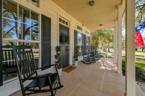 A covered porch with black rocking chairs, a Texas flag, and a view of the surrounding trees.