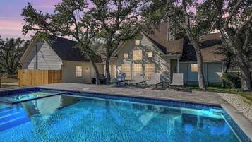 Ein Wohnhaus mit Swimmingpool, einer überdachten Terrasse mit Liegestühlen und einem Holzzaun.