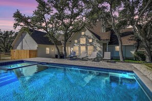 A residential property with a swimming pool, a covered patio with lounge chairs, and a wooden fence.