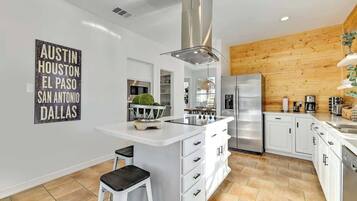 Une cuisine moderne avec des meubles blancs, un îlot central, des appareils en acier inoxydable et un mur d’accent en bois.