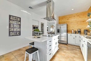 A modern kitchen with white cabinetry, a central island, stainless steel appliances, and a wooden accent wall.
