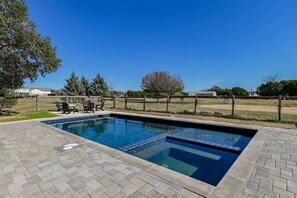 A rectangular swimming pool with a tiled edge, surrounded by a brick patio.