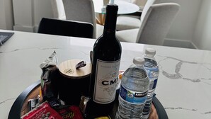 Une table à manger avec une bouteille de vin, des bouteilles d’eau, des en-cas et une petite plante.