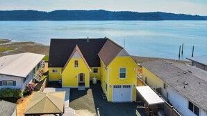 Une maison jaune avec un garage et un patio couvert, située près d’une étendue d’eau.