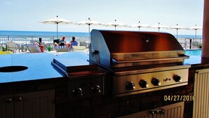An outdoor grill area with a view of the ocean and beach umbrellas.