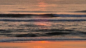 A sunset over the ocean with waves approaching the shore.