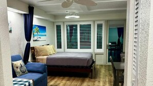 A compact bedroom with a bed, a small sofa, a dining table, and a ceiling fan.