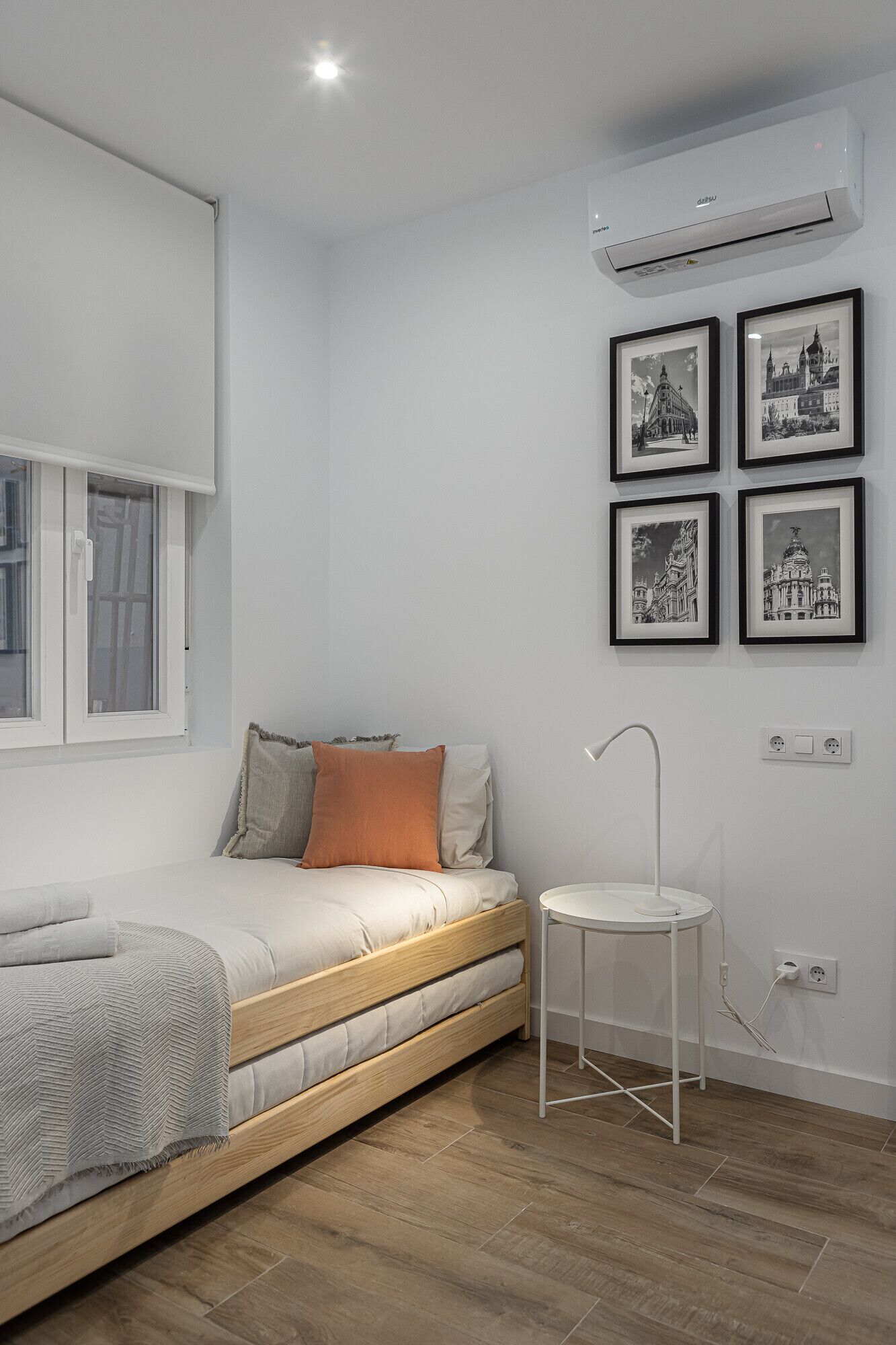 Quarto minimalista com uma cama, uma mesinha de cabeceira e um ar condicionado fixado na parede.