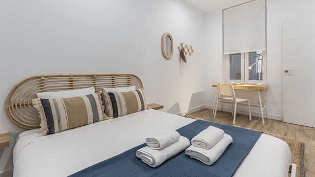A bedroom with a bed, a desk, a chair, a mirror, and a door. - Waou Coosy II Retiro (Madrid)