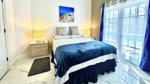 A bedroom with a bed, bedside lamps, a nightstand, a painting, and a window with curtains. - Comfy Home Near Theme Parks (Kissimmee)