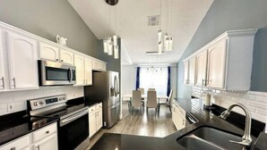 A modern kitchen with white cabinets, stainless steel appliances, and a black countertop. - Comfy Home Near Theme Parks (Kissimmee)