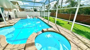 A swimming pool with a glass enclosure, surrounded by a brick deck and a grassy yard. - Comfy Home Near Theme Parks (Kissimmee)