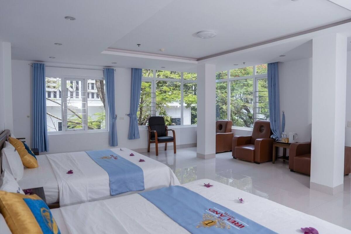 Ein Hotelzimmer mit zwei Betten, einer Sitzecke mit Sesseln und großen Fenstern mit Blick auf Grünflächen.