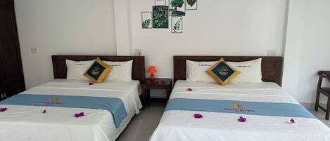 A hotel room with two beds, each with a pillow featuring a logo, a nightstand with a lamp, and a wall decorated with framed pictures.