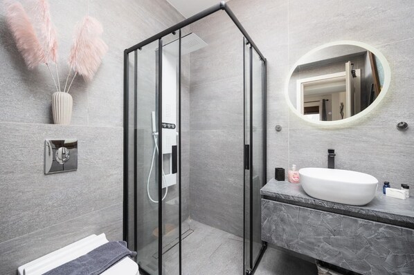 Une salle de bain moderne avec une douche à l’italienne en verre, un lavabo en marbre et un miroir rond.