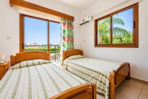 Un dormitorio con dos camas, ventanas amplias, equipo de aire acondicionado y vista a zonas verdes.