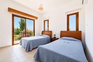 Habitación de hotel con dos camas, un balcón y vistas al verdor.