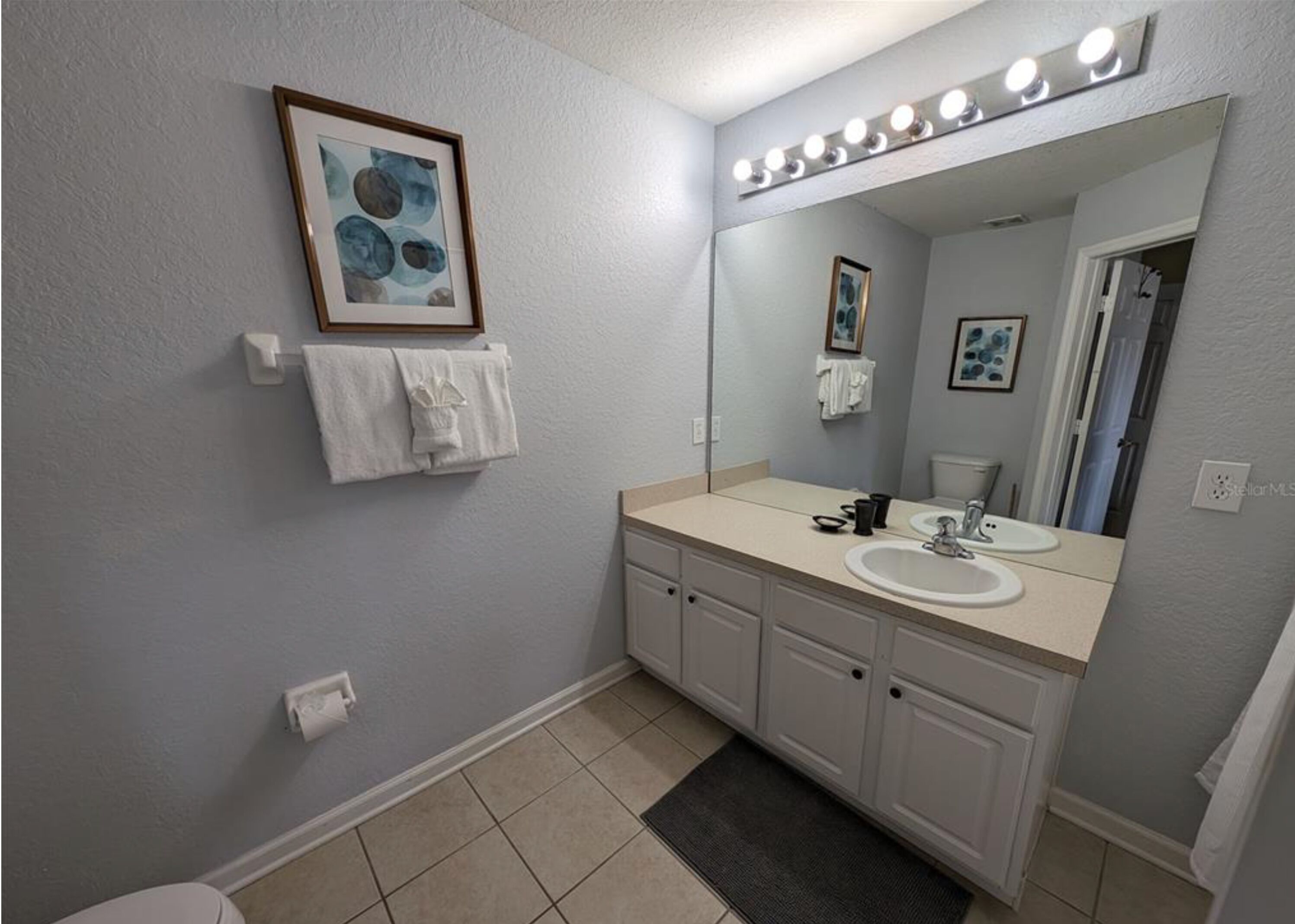A bathroom with a large mirror, two sinks, and a towel rack.