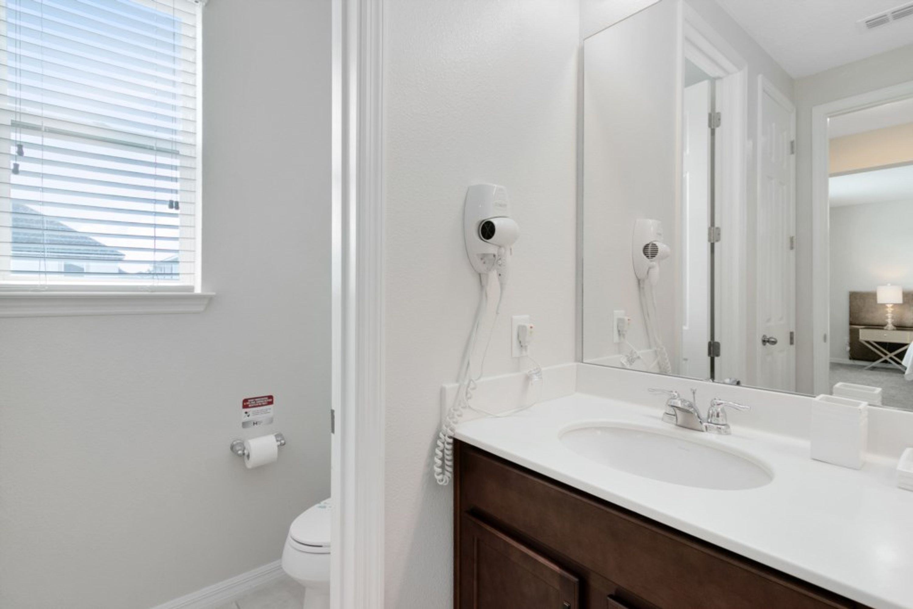 A modern bathroom with a white sink, a large mirror, and a hairdryer mounted on the wall.