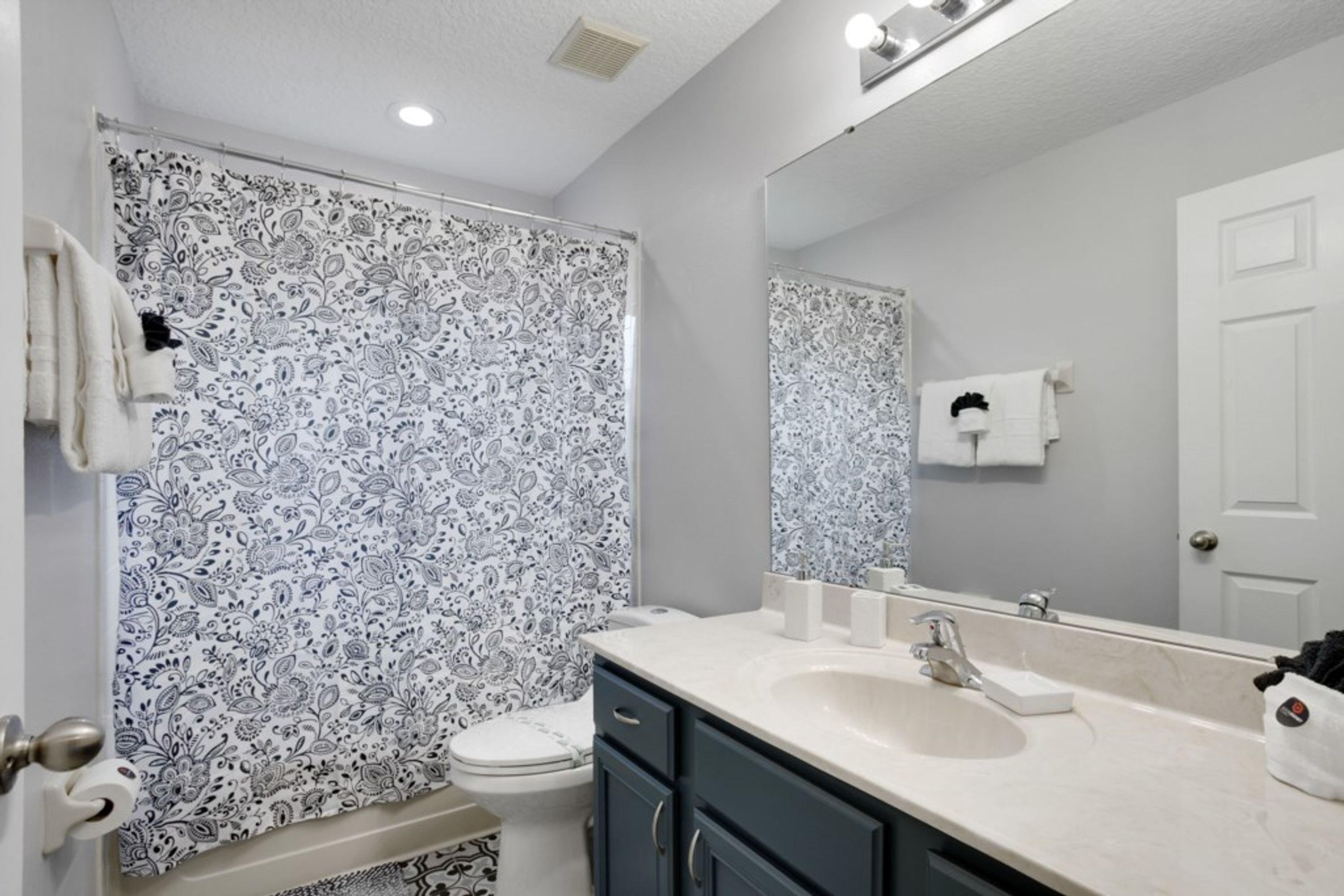 A bathroom with a patterned shower curtain, a sink, a mirror, and a toilet.