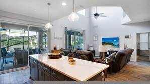 Un vaste espace de vie comprenant un grand îlot central, un canapé en cuir foncé et une table à manger. On y trouve également plusieurs ventilateurs de plafond et des luminaires suspendus.