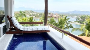 A balcony with a pool, a lounge chair, and a view of a coastal area with mountains and buildings. - Villa Frente al Mar con Hermosas Vistas (Ixtapa)