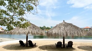 A beach with thatched umbrellas and wooden chairs. - Villa Frente al Mar con Hermosas Vistas (Ixtapa)