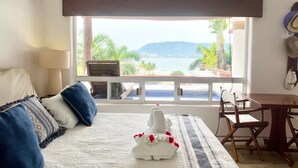 A bedroom with a bed, a table, and a view of a pool and mountains. - Villa Frente al Mar con Hermosas Vistas (Ixtapa)