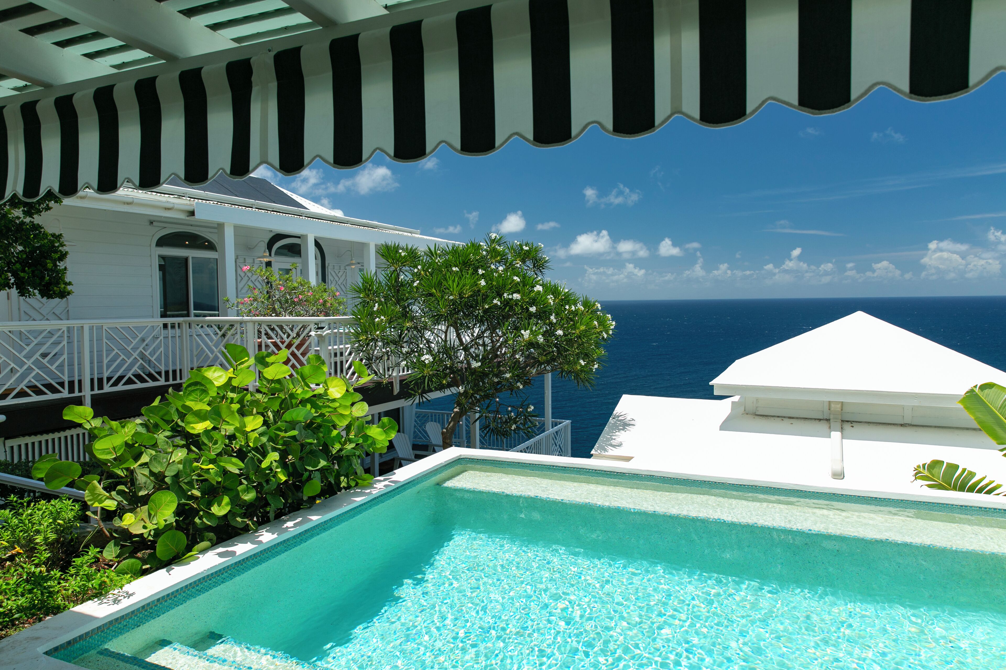 Une piscine avec vue sur l’océan, un bâtiment blanc doté d’un balcon et une végétation luxuriante.
