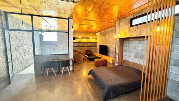 A cozy room with a brick wall, a wooden ceiling, a bed, a TV, and a seating area with a chair and a small table.