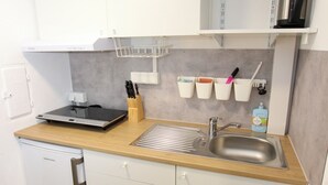 Een kleine keuken met witte kastjes, een roestvrijstalen spoelbak, een koffiezetapparaat en een afdruistraal.