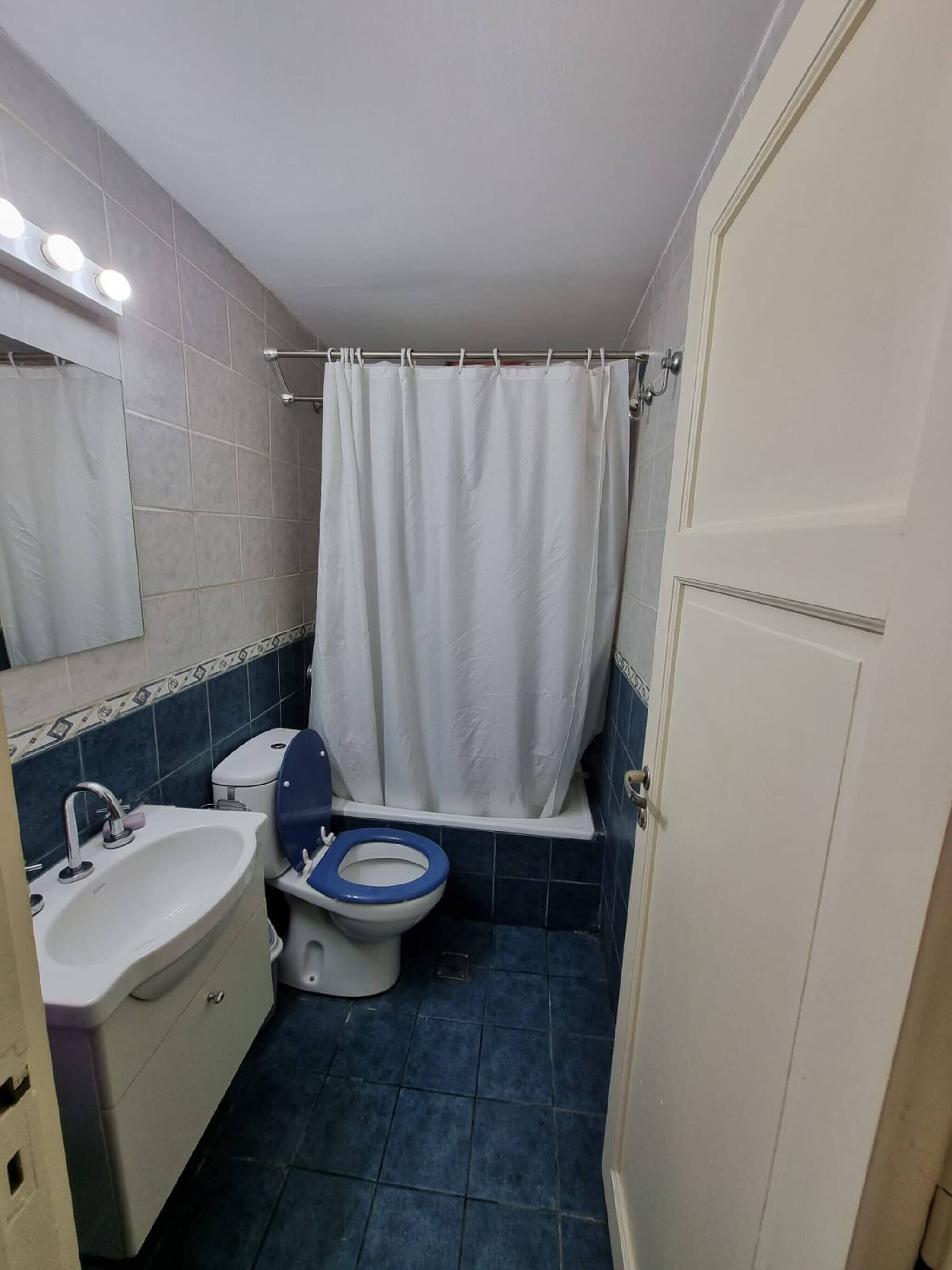 A bathroom with a white sink, blue toilet, and a shower curtain.