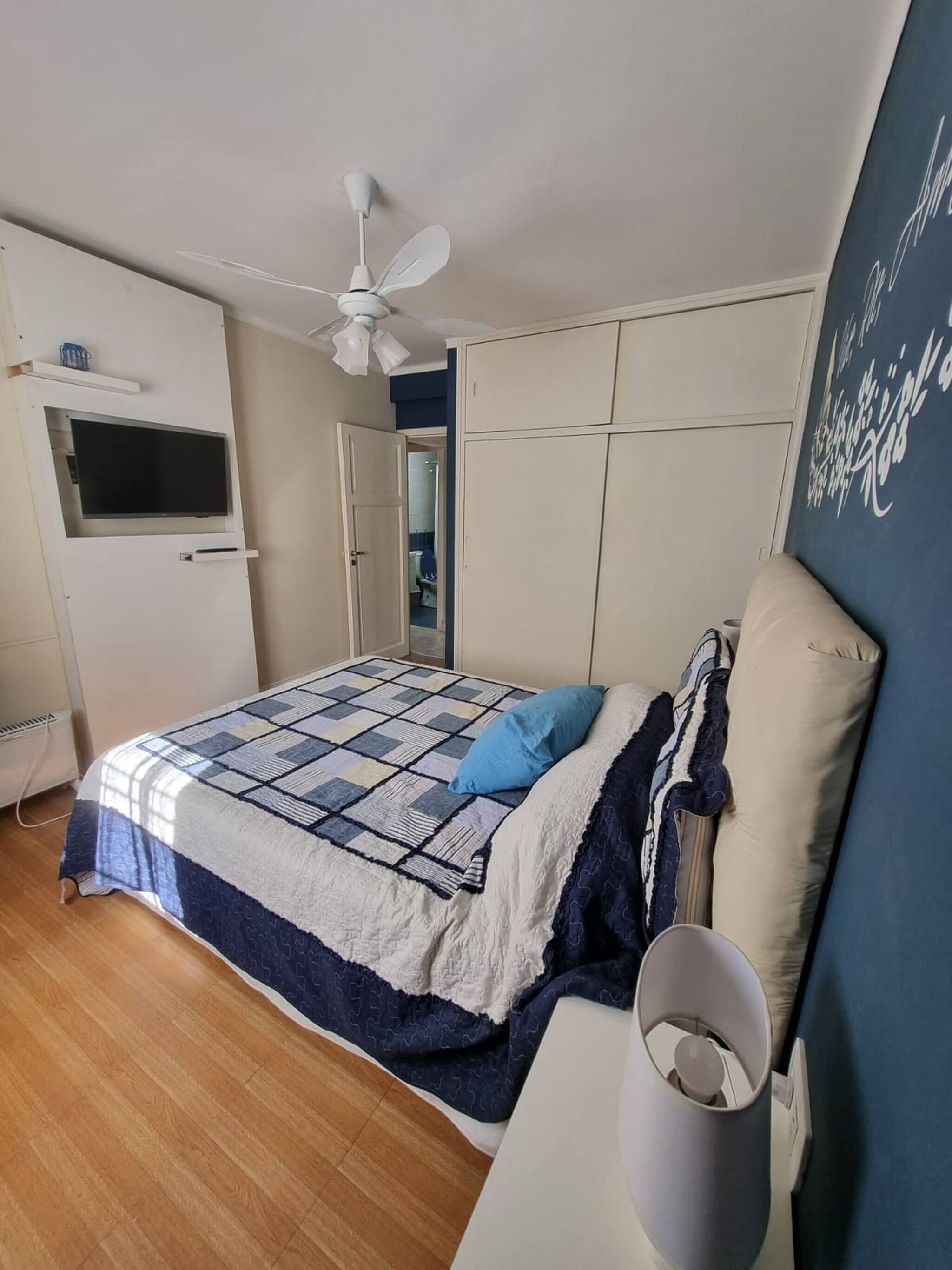 A bedroom with a bed, a ceiling fan, a TV mounted on the wall, and a wardrobe.
