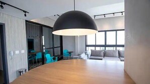 A modern conference room with a large wooden table, a black dome-shaped pendant light, and a sofa with cushions. - Studio 309 WBE São Paulo prx PUC Allianz (São Paulo)