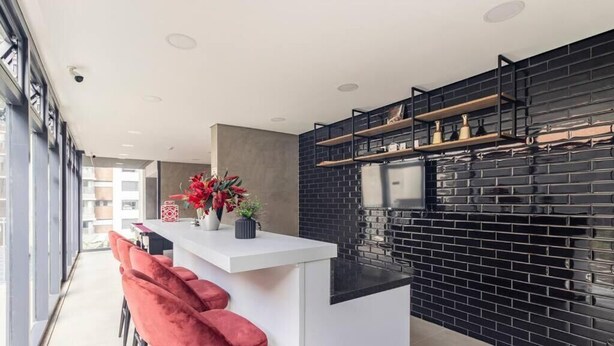 A modern kitchen with a black tiled backsplash, white countertops, and red bar stools. - Studio 203 São Paulo prox Allianz Unimed (São Paulo)