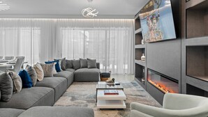 Un salon moderne avec un canapé d’angle, un téléviseur à écran plat, une cheminée et un coin repas à l’arrière-plan.