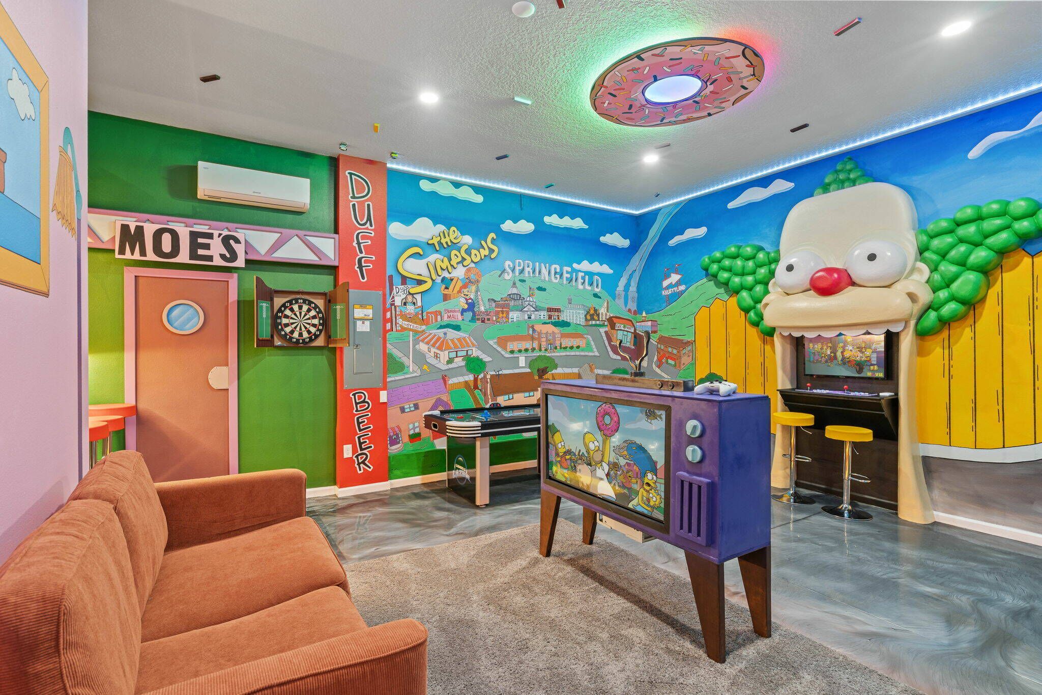 Ein Zimmer mit Dartscheibe, Fernseher und einer Wandmalerei von Springfield.