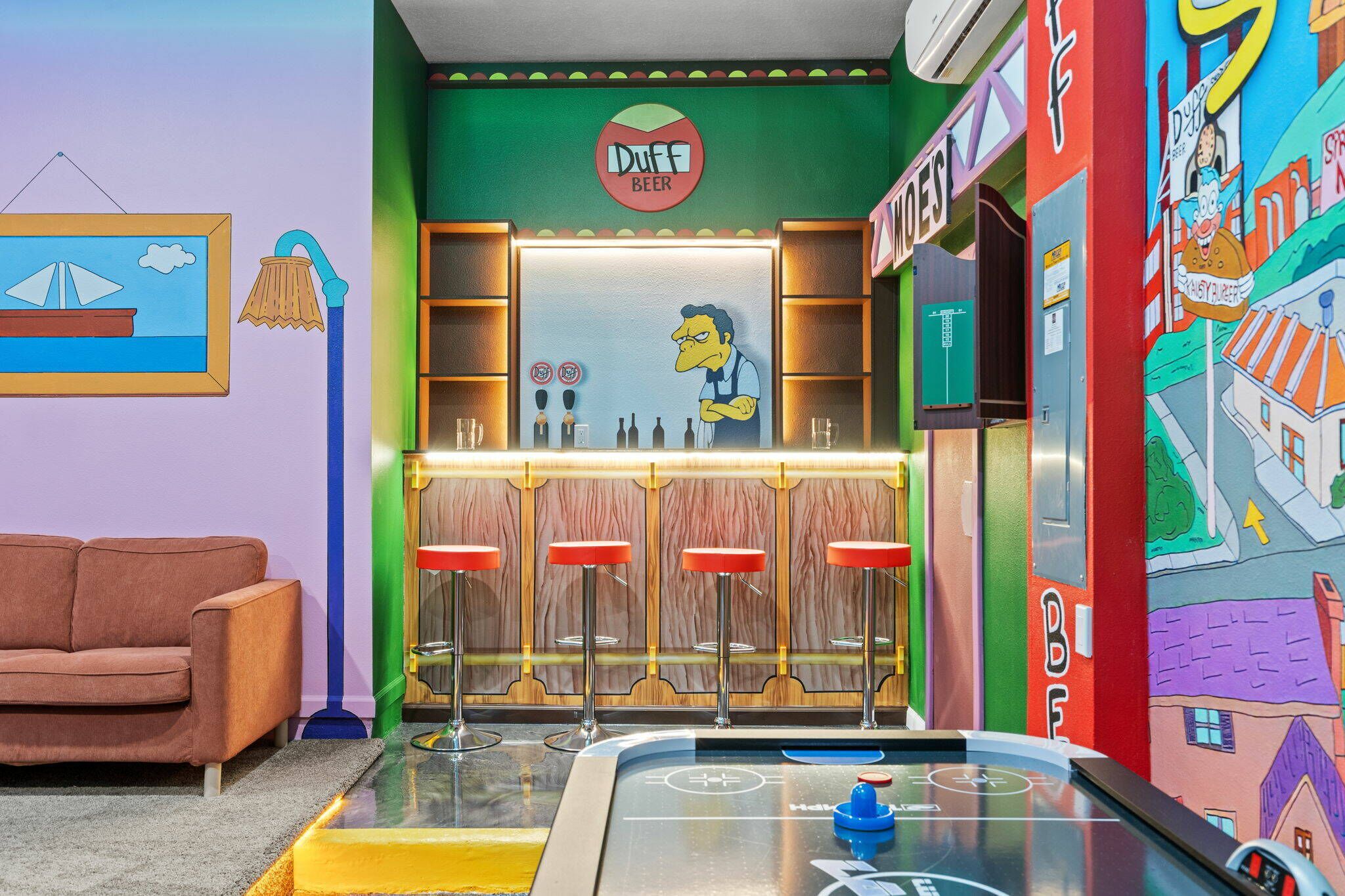 A bar area with a Duff Beer sign, bar stools, and a pool table.
