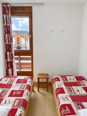 A room with two beds, a wooden bench, and a window with curtains.