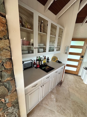 A kitchen with white cabinets, a stone wall, and a countertop with bottles and a coffee maker. - New rental, Newly Renovated 3br/2ba - open main room/beautiful view/large pool  (Cruz Bay)