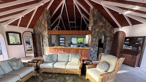 A spacious living area with a stone fireplace, a wooden ceiling, and a view of the kitchen. - New rental, Newly Renovated 3br/2ba - open main room/beautiful view/large pool  (Cruz Bay)