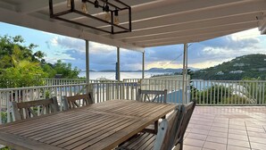 A wooden table and chairs under a covered patio with a view of a body of water and hills. - New rental, Newly Renovated 3br/2ba - open main room/beautiful view/large pool  (Cruz Bay)